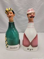 Front view of two porcelain decanters shaped as men, one green labeled 'Scotch' the other pink labeled 'Rye'