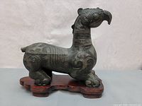 Side view of the bronze dragon figurine on wooden base showing engraved patterns and form.