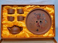 Full view of the Yixing tea set with teapot, four cups, and the painted round tray inside a display box with yellow silk lining.