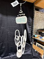 Full view of a white ceramic wind chime with teal turtle design hanging against a black background.