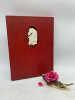 Red Boehm collector book with white horse emblem and porcelain Rose of Hope figurine showing broken detached petal