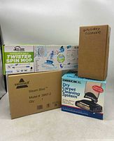Photo of all four boxed items: Eco+Home rechargeable Twister Spin Mop, Bissell Steam Shot steam cleaner, Oreck Dry Carpet Cleaning System, and upholstery cleaner in plain box.