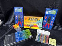 Wide view of all items in the lot showing the MFK central door lock box, crimping tools on cards, mounting wire kit, and sealed strip of small parts.