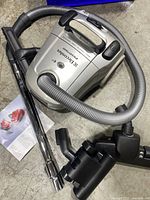 Silver Electrolux Essensio vacuum cleaner with handle, hose, extension tubes, black floor nozzle, manual and accessories on concrete floor
