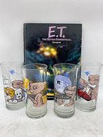 Four vintage Pizza Hut E.T. collector glasses arranged in front of a hardcover E.T. storybook showing front cover.