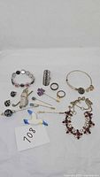 Full overview of the costume jewelry lot including bracelets, stick pins, rings, and necklace displayed on white surface with lot number card.