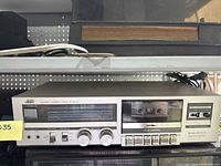 Front view of JVC stereo cassette deck showing control knobs and cassette compartment with tape inside.