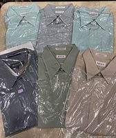 Six green toned men's dress shirts folded and wrapped in packaging, shown from top collar view.