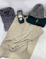 Overview of lot showing plaid shirt, beige sweater, green cable knit sweater, gray beanie, and watch in box.