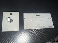 Two pieces of jewelry from Primrose shown on branded display cards: a sterling silver ring with a flower and clear stone, and a sterling silver choker chain with extender.