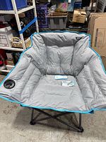 Front view of large padded grey chair with blue trim featuring cup holder and quilting design.