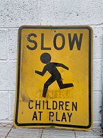 Front view of vintage yellow metal street sign with black text and running child graphic.