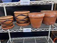 Four terra-cotta pots displayed on a metal shelf, two with blue wavy patterns and two plain. All have matching saucers; one plain pot shows a crack.