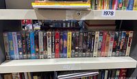 Shelf of VHS movies dated 1978 shows various titles packed tightly on one shelf, all shrink wrapped as new old stock.