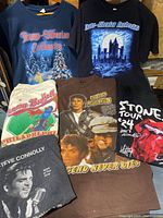 Six vintage music t-shirts laid out, showing graphics and conditions.