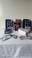 Wide view of three metal storage tins and one white cardboard box containing hockey trading cards spread out on a white cloth.