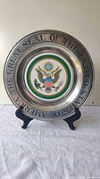 Front view of the commemorative plate showing the Great Seal of the United States and the embossed text on silver metal rim.