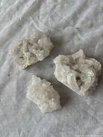 Top view of three small clear/white quartz crystal clusters laid on a white cloth surface.