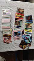 Photo of over 200 assorted trading cards spread in several stacks on a white surface. Cards feature varied pop culture themes with colorful, detailed artwork and photographs.