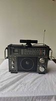 Full front view of black Venturer VU-660 multiband receiver cassette player with speaker, tuning meter, control knobs, side handles, and telescoping antenna extended.