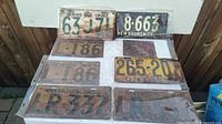 Photo showing all license plates laid out on a white table, including Ontario plates dated 1941 and New Brunswick plate dated 1939, all with visible rust and wear.