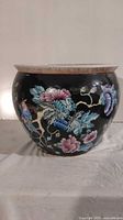 Side view of vintage oriental ceramic planter showing black background with colorful floral and bird design.