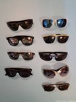 9 pairs of men's sunglasses laid out on a surface showing variety of frame styles and lens colors including black, brown, and mirrored blue.