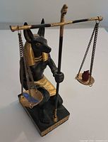 Black and gold Anubis statuette holding scales with feather and heart
