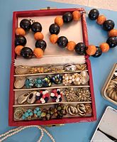 Photo showing red vintage box with multiple pairs of colorful clip-on earrings, bracelets, costume rings and large bead necklace