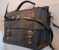 Black leather laptop bag front with dual buckle straps and shoulder strap