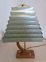 Front view of sage green metal slat pyramid lamp shade on a wooden lamp base, showing feathered motif and stepped design.