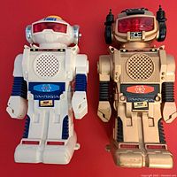 Front view of white and gold New Bright Model-B robots showing chest speaker, eye covers, and body details.
