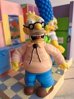 Close-up image of Grandpa Simpson talking figure, wearing glasses and pink sweater