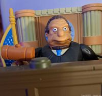 Close-up of judge figure holding gavel behind courtroom bench showing detailed facial expression and accessories