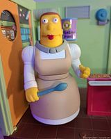 Close-up image of Lunch Lady Doris figure holding a large blue spoon inside the cafeteria playset, showing detail of character and set interior.