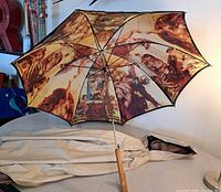 Black umbrella opened showing the full Sistine Chapel ceiling art on the interior canopy along with the beige rain poncho folded on the table.