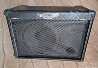 Front view of the Traynor TMV50 speaker showing the metal grille and logo, with visible signs of wear on the cabinet edges.