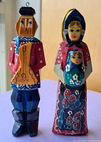 Close-up of two smaller wooden ornaments: a man playing a string instrument and a woman holding a child, painted in traditional Russian style