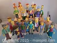 Group of 21 Simpsons character figures including Luigi, Lionel Hutz, Artie Ziff, Ms. Botz, Gil, and others arranged together.