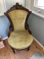 Front angled view of green velvet vintage accent chair showing carved wooden frame and worn upholstery.