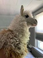 Side view of the alpaca puppet showing curly cream and brown alpaca fur and realistic fabric face with ears and eyes.
