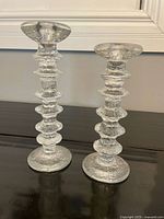 Front view showing pair of textured clear glass candlesticks of two heights on a dark surface.