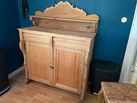 Full view of the cabinet showing two doors, two drawers, and upper decorative shelf in stripped natural wood finish