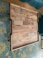 Top view of square distressed wood coffee table showing wood grain and two wrought iron handles on opposite sides.