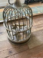 Front side view of the small brass birdcage showing hook on top, swinging perch, and vertical bars.