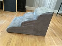 Side angled view of gray foam pet stairs showing three steps and triangular foam base on wooden floor