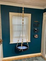 Photo showing the large black wicker hanging tray suspended in front of a window, tied with macramé rope and wooden beads.