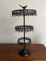 Front view of the black metal 3-tiered jewelry stand showing ornate design and bird figurine topper.