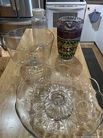 Full view of four items on table: clear glass trifle bowl, clear ribbed glass pitcher with white lid, colored textured glass pitcher, and clear glass cake plate.