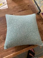 Top view of square teal pillow with white dash pattern on wooden surface.